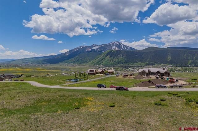 Green valley with a mountain range, cloudy blue sky, and a small cluster of houses and roads in the foreground.
