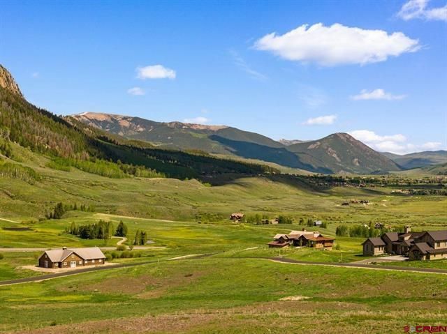 Green mountain valley with scattered houses under a blue sky and clouds