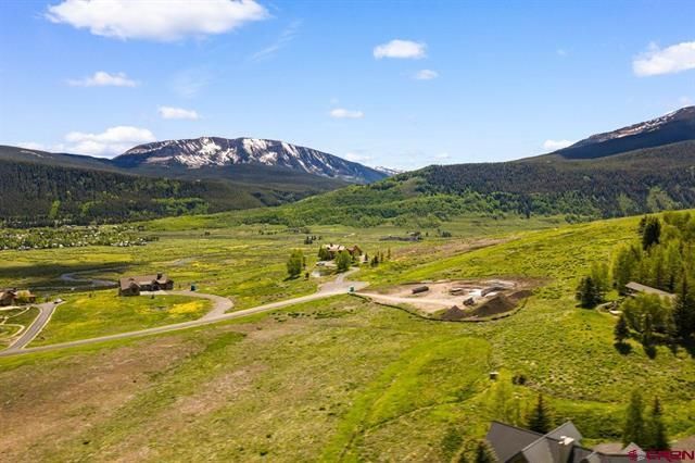 Wide green mountain valley with snow-capped peaks, blue sky, and scattered homes near a winding road