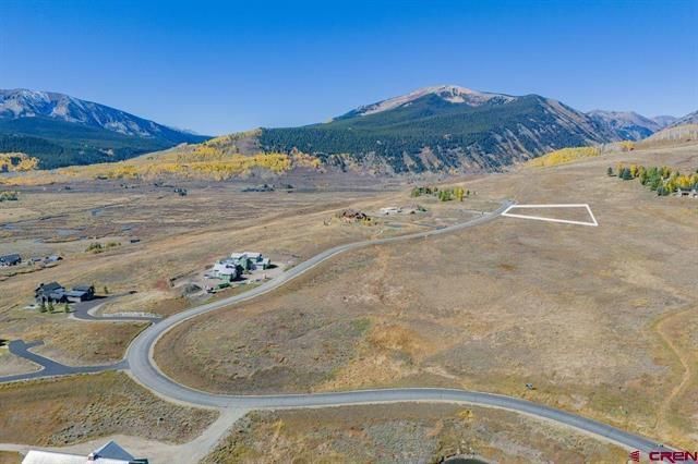 Rural hillside lot outlined in white beside winding road, with mountains and open fields in the background