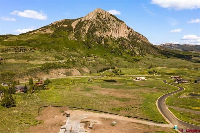 Green valley with a rocky mountain under a partly cloudy sky and a winding road in the foreground