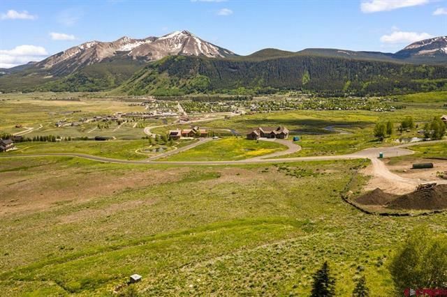 Green valley with a winding dirt road leading to snow-dusted mountains under a blue sky