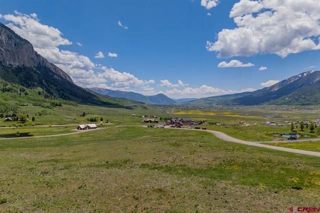 Wide alpine valley with green meadows, mountains, scattered houses, and a blue sky with clouds