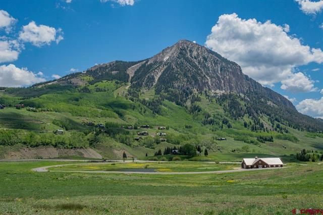 Green valley with a rocky mountain under a blue sky, with small buildings in the foreground