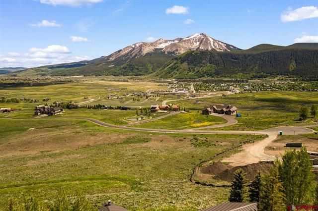 Mountain landscape with green valley, winding dirt road, and snow-dusted peak under a blue sky
