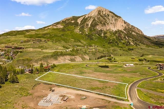 Mountain landscape with terraced green hills, a rocky peak, and a winding road under a blue sky