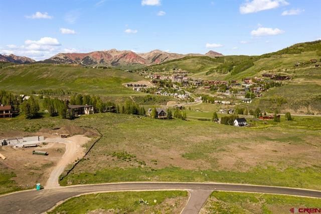 Wide green valley with winding road, scattered houses, and red hills under a blue sky