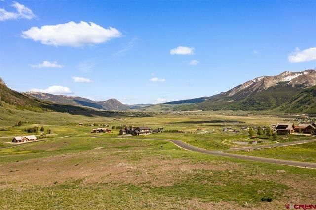Wide grassy valley with a winding road, scattered houses, and mountains under a blue sky