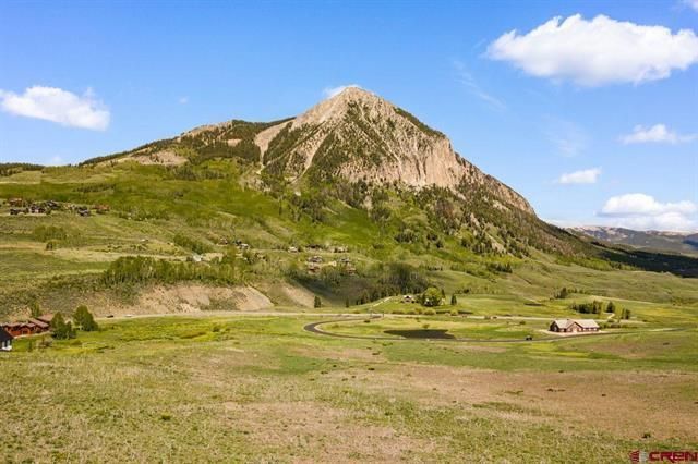 Grassy plain with a rocky mountain under a blue sky and scattered clouds