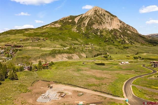 Green valley with a rocky mountain under a blue sky, winding road, and scattered fields