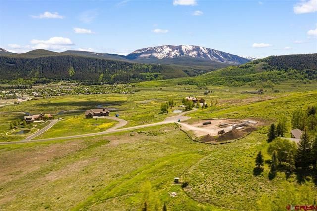 Mountain valley with green fields, scattered cabins, and a snow-capped peak under a clear sky