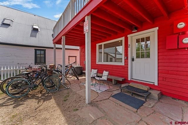 Red building entrance with white door, bench, bikes, and stone patio under a covered porch