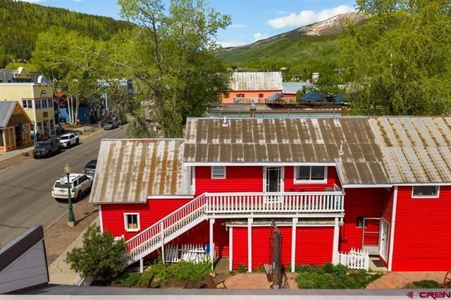 Red building with white trim and stairs beside a street, with trees and hills in the background.