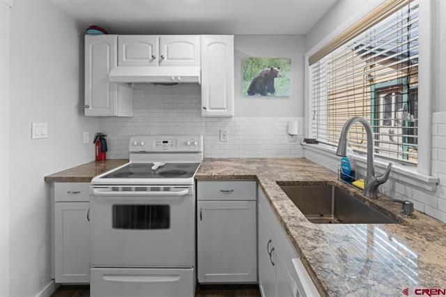 Bright white kitchen with stove, cabinets, granite counters, and a window over the sink