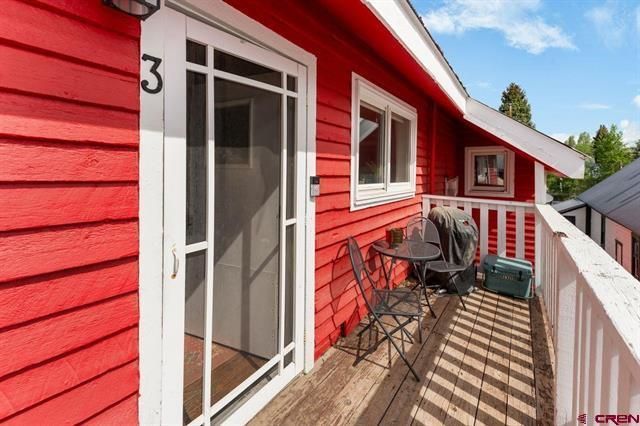 Red balcony with chairs and table beside red house, overlooking trees and neighboring homes.
