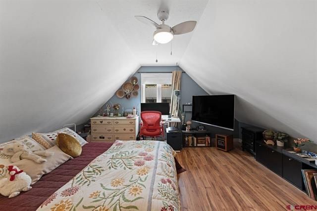 A cozy attic bedroom with a bed, dresser, TV, and sloped white ceiling.