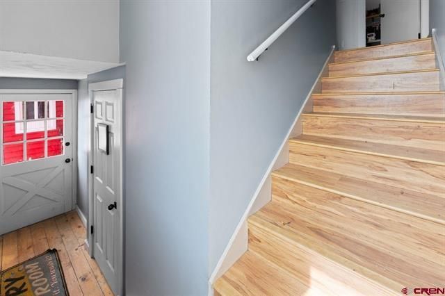 Interior staircase with light wood steps, pale blue walls, and a front door with a red-paneled window.