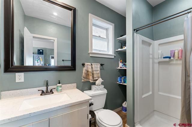 Small blue bathroom with vanity, toilet, shower, mirror, and window