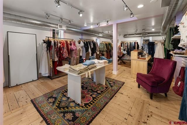 Boutique clothing store interior with racks of dresses, a display table, and a purple armchair