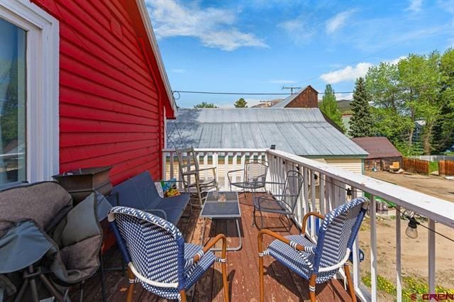 Balcony with blue chairs and small table beside a red house, overlooking rooftops and trees