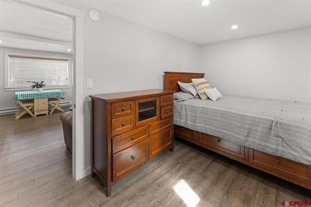 Small bedroom with wooden dresser, bed, and a doorway to a bright dining area