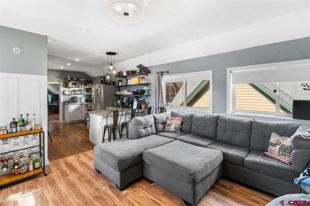 Bright living room with gray sectional sofa, wood floors, and kitchen bar in the background