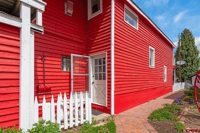 Red house exterior with white trim, picket fence, and garden path by an open side door