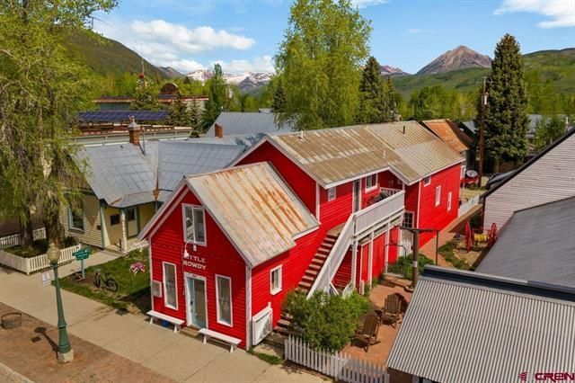 Red barn-style buildings in a mountain village with trees and blue sky