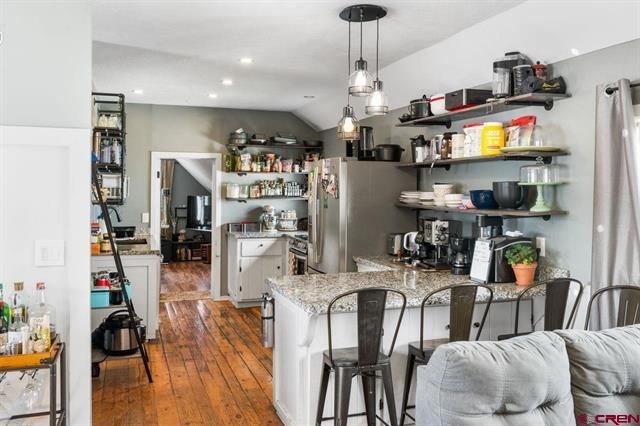 Modern kitchen with gray island, hanging lights, open shelves, and hardwood floors