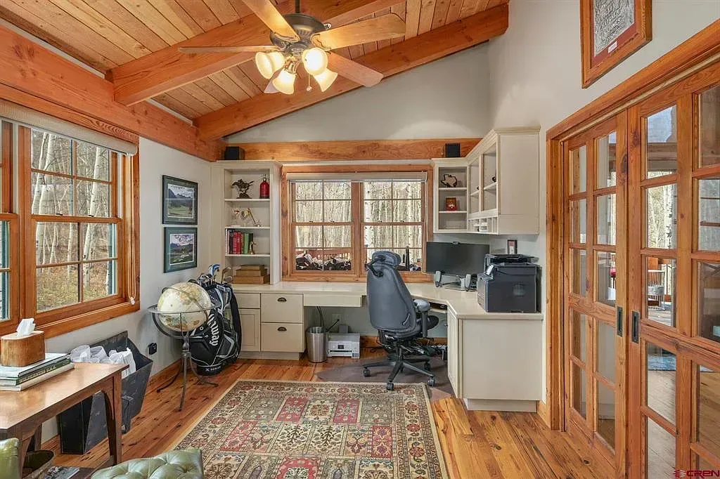 Bright home office with wood ceiling, large windows, desk, chair, rug, and built-in shelving