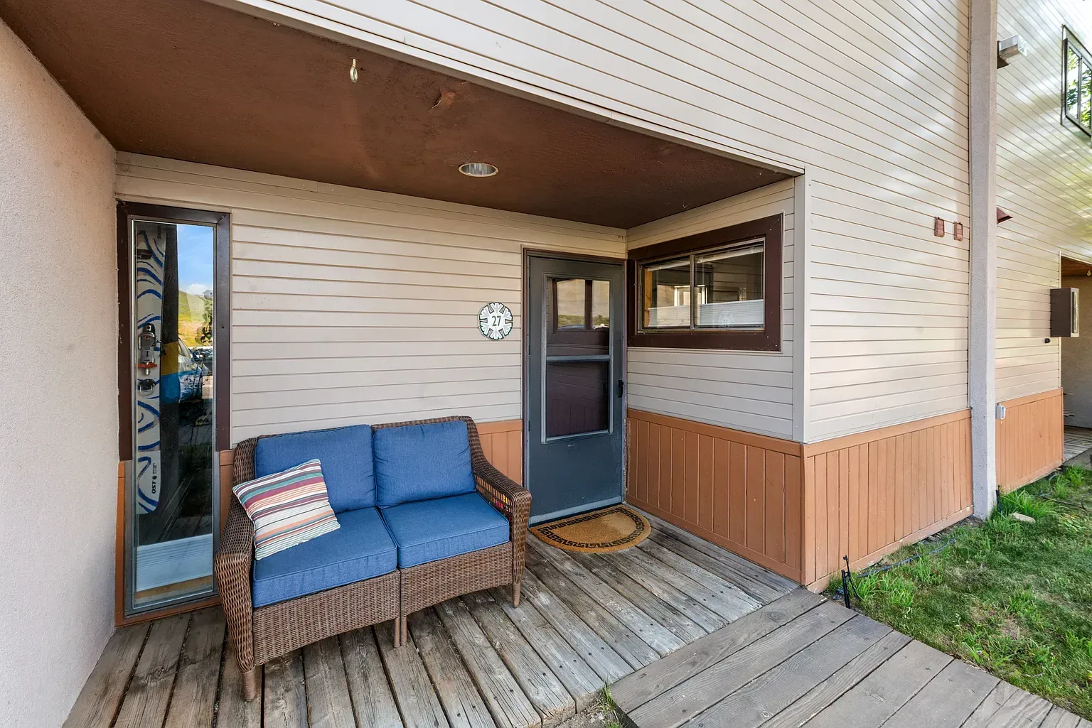 Covered porch with blue bench, wood siding, and front door beside a small window
