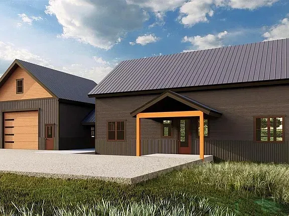 Modern house with dark siding and metal roofs beside a garage, under a blue sky with clouds