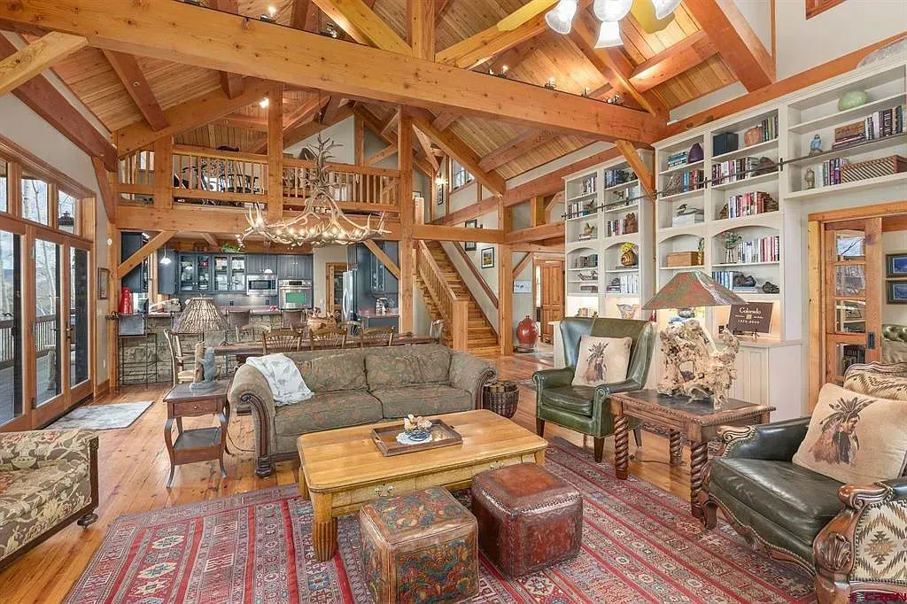 Cozy rustic living room with wood beams, patterned rugs, upholstered chairs, and a central coffee table