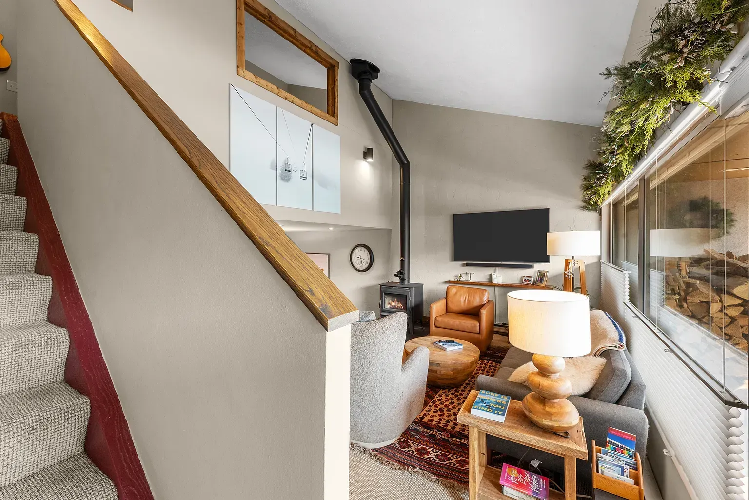 Cozy living room with tan sofa, wall-mounted TV, staircase, and window seat by the fireplace