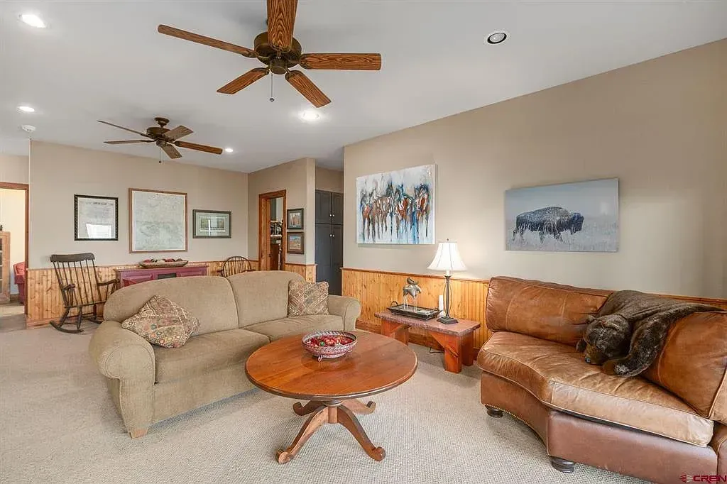 Cozy living room with tan and brown sofas, ceiling fans, and warm wall art.