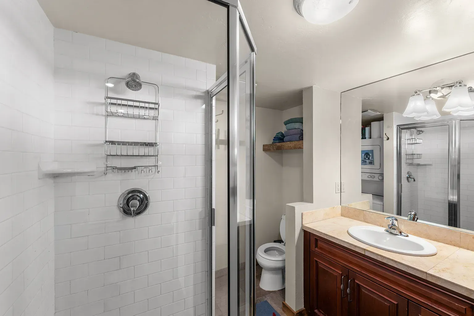 Bathroom with glass shower, white tile, toilet alcove, and dark wood vanity with sink.