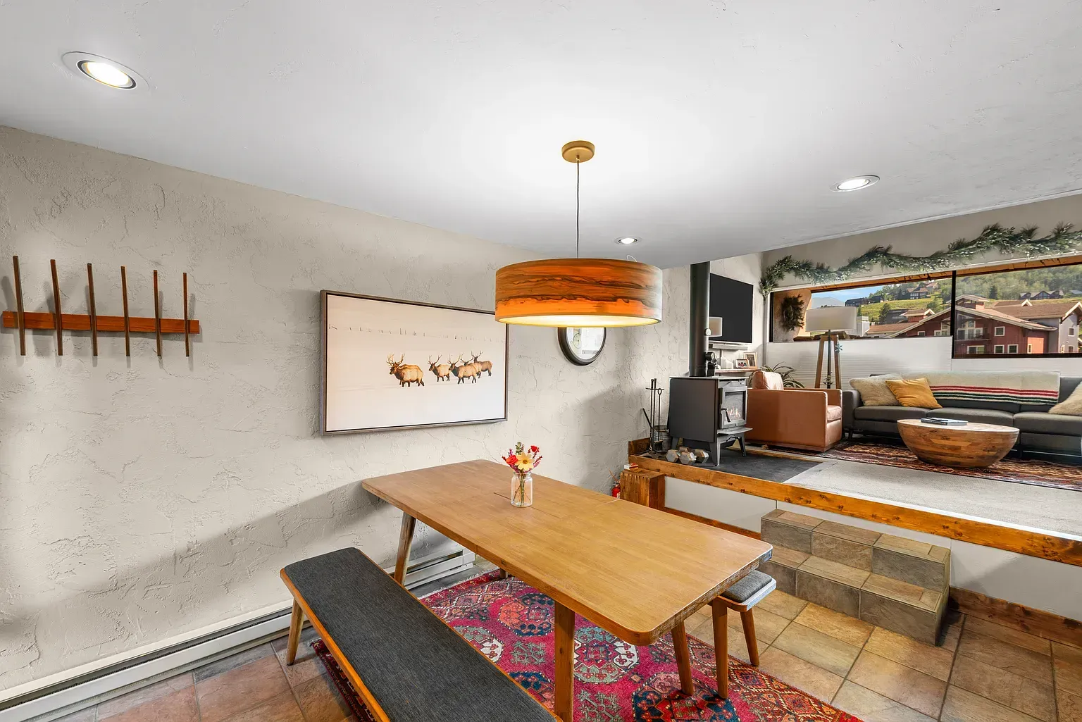 Modern dining area with wooden table, bench seating, orange pendant light, and wall art in a bright room