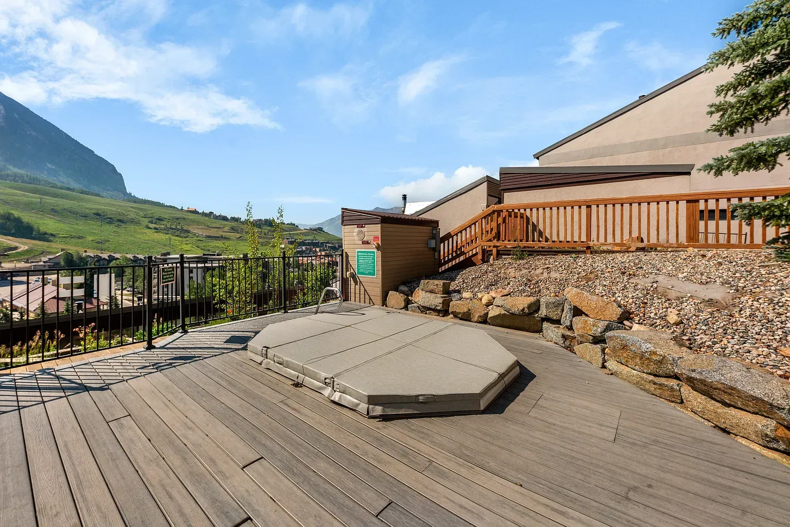 Wooden deck with hexagonal fire pit, stone wall, and mountain view under blue sky