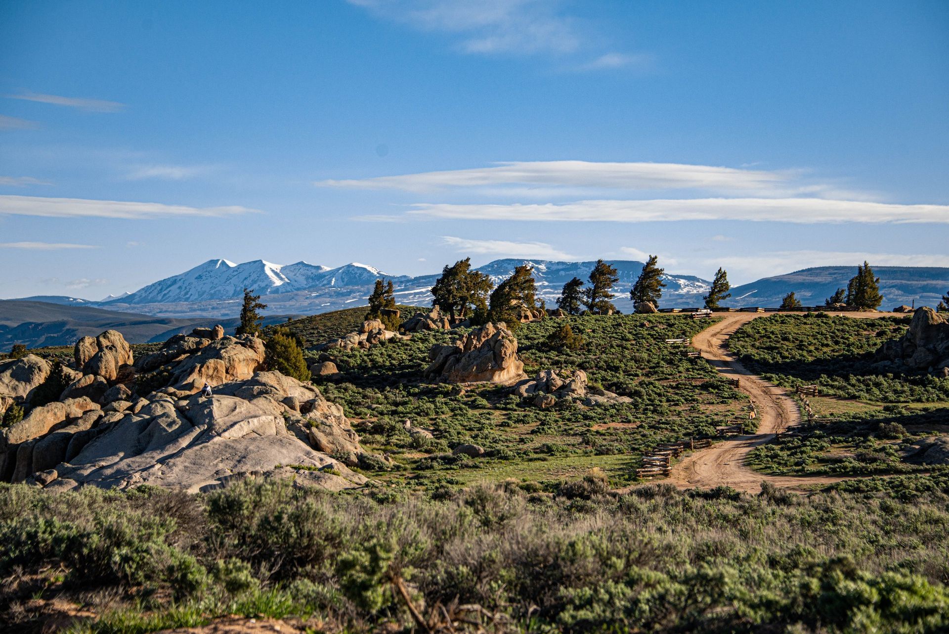 Rocky trail through a green valley with snowcapped mountains under a blue sky