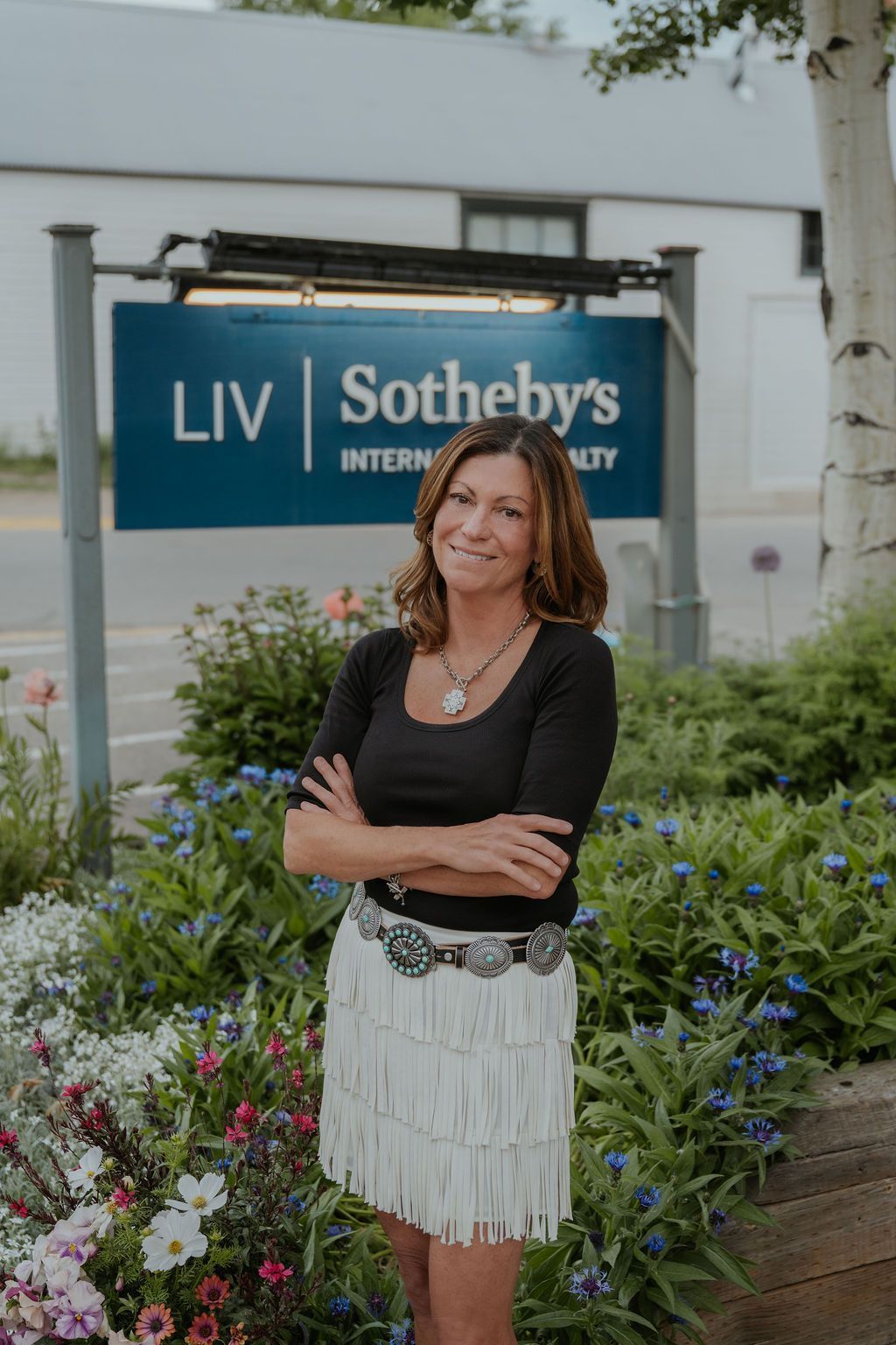Woman standing outdoors in front of a LIV Sotheby’s International Realty sign, arms crossed and smiling.