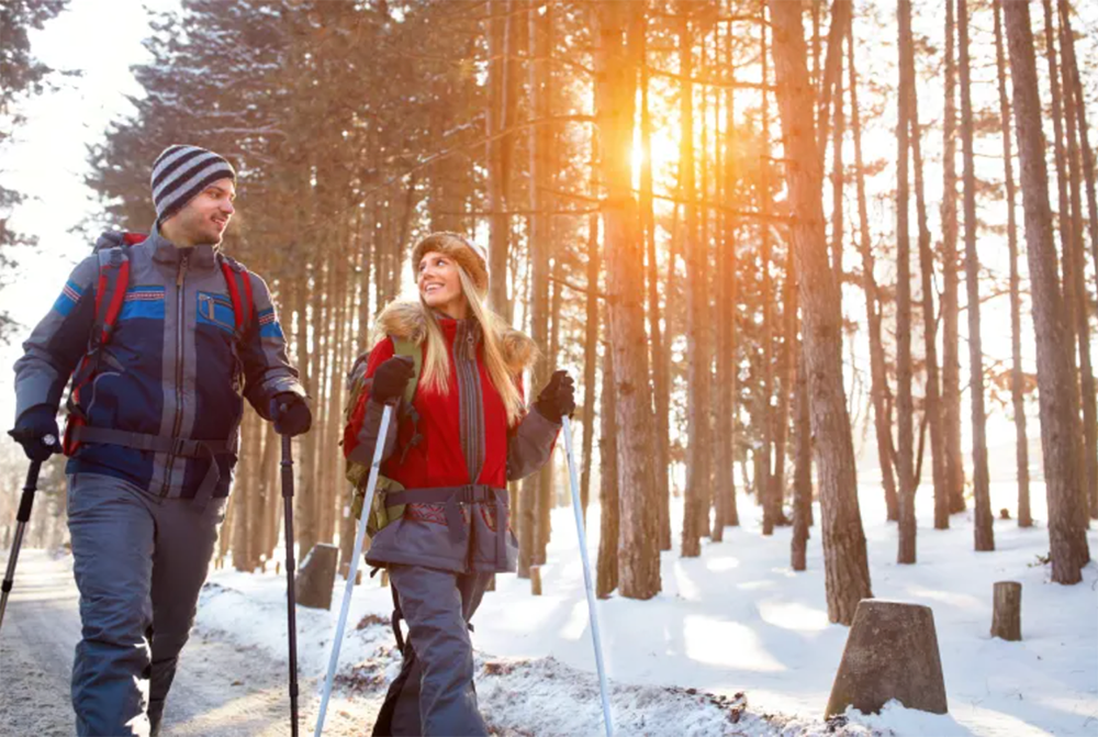 Two hikers walking through a snowy forest at sunset with warm sunlight through the trees