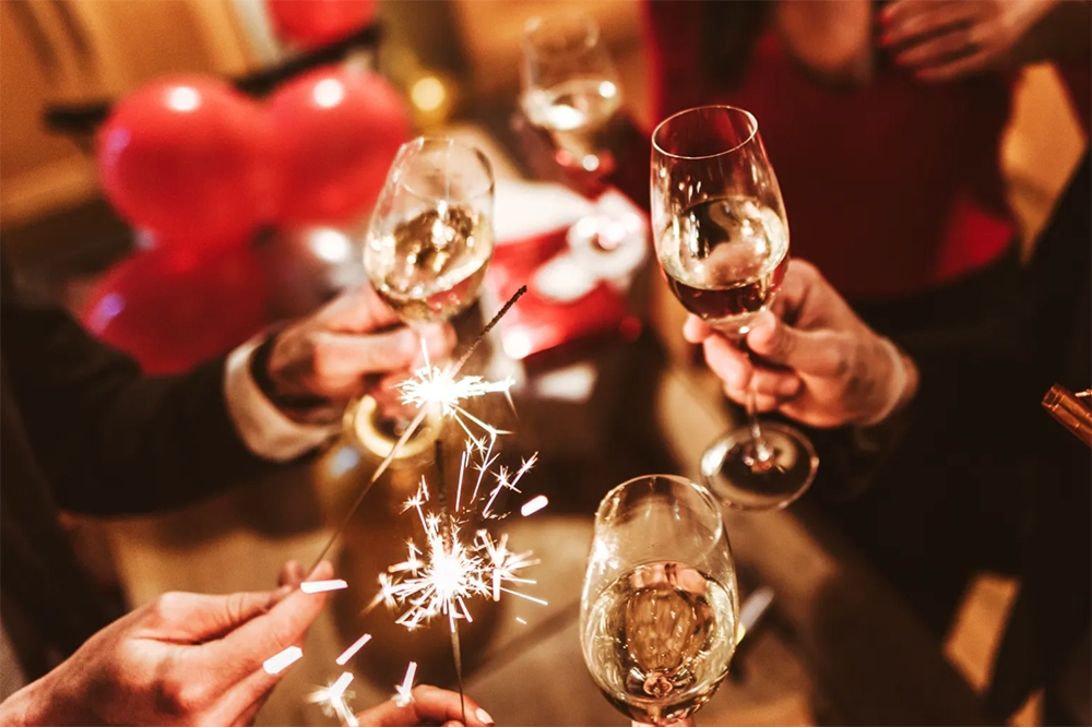 Hands holding champagne glasses and sparklers at a warm, festive party