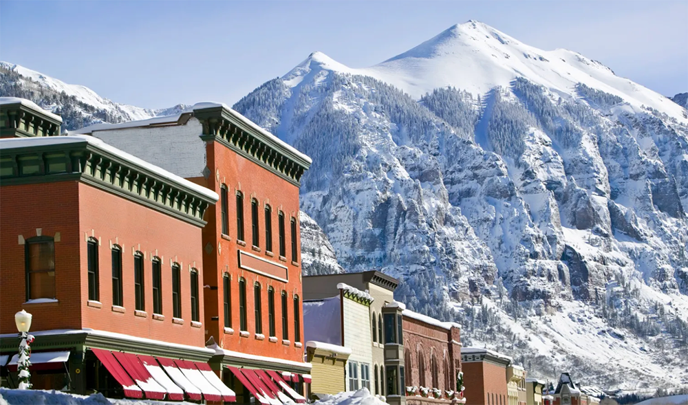 Red brick storefronts beneath snow-covered mountains in a winter town