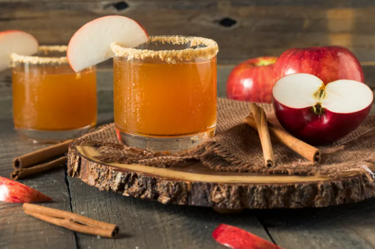 Apple cider in glasses with cinnamon sticks and sliced apples on a rustic wooden table