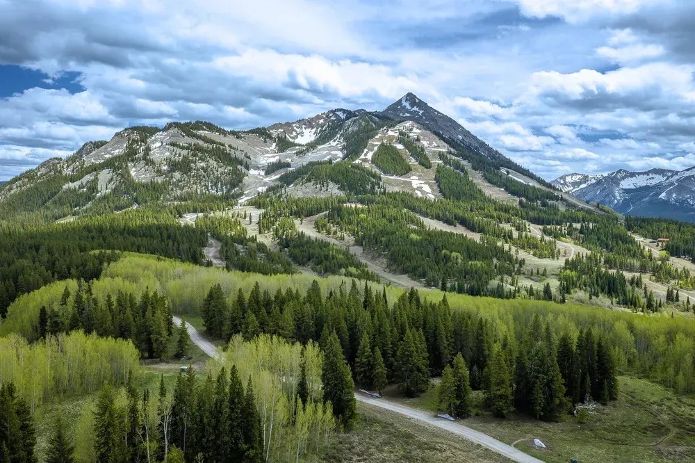 Mountain landscape with green forest, rocky peaks, and a cloudy blue sky
