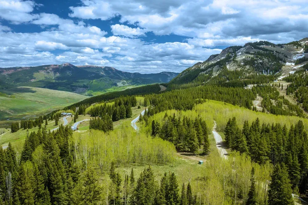 Mountain valley with green forests and meadows under a partly cloudy blue sky