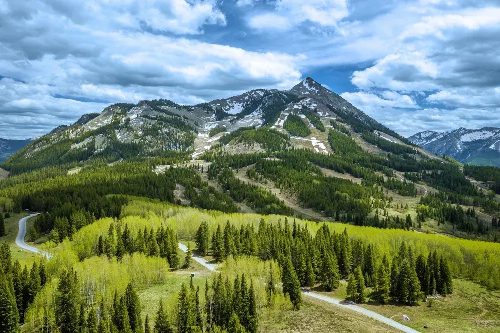 Mountain landscape with green forest, rocky peaks, and cloudy sky