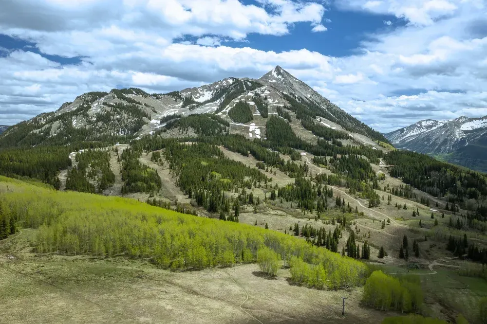 Mountain landscape with green slopes, rocky peaks, and a cloudy blue sky