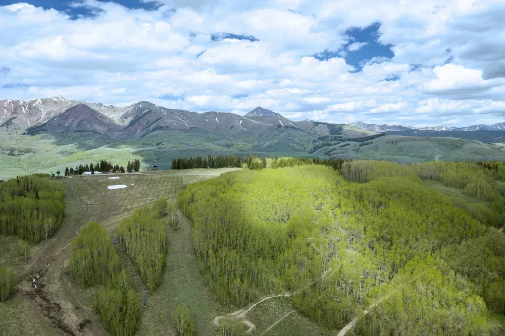 Aerial view of green forested hills and mountains under a blue sky with scattered clouds