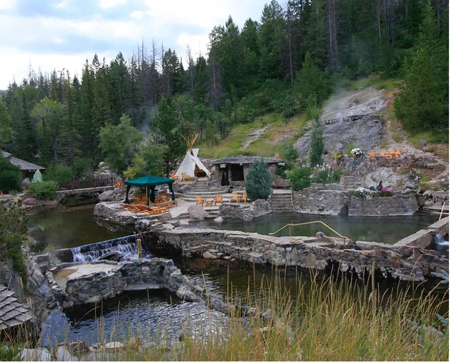 Small stone pool and waterfall in a forested rocky landscape with a gazebo and picnic area